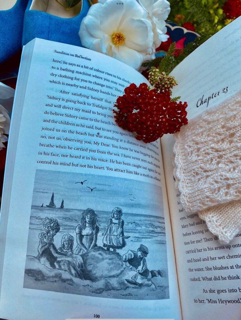 Open book displaying a gray illustration of children playing at the beach beneath Chapter 23, surrounded by flowers and blue shoes.